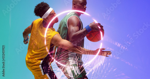 African american basketball players defending ball from opponent by illuminated circle and plants