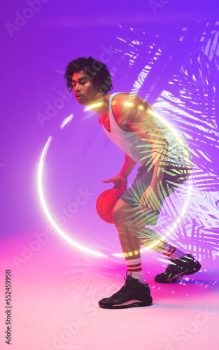 Side view of male biracial player dribbling basketball by illuminated plants and circle, copy space