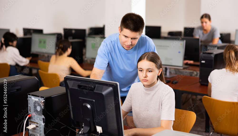 Fototapeta premium Focused boy helping young female student working with pc in library computer room