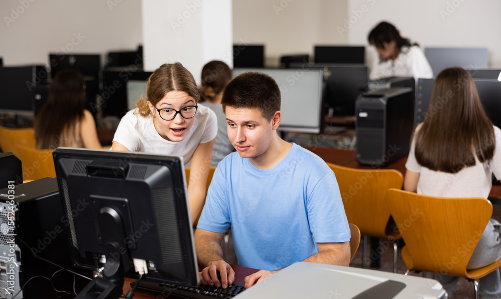 Fototapeta premium Teenager girl helps friend solve problem on computer in a school class
