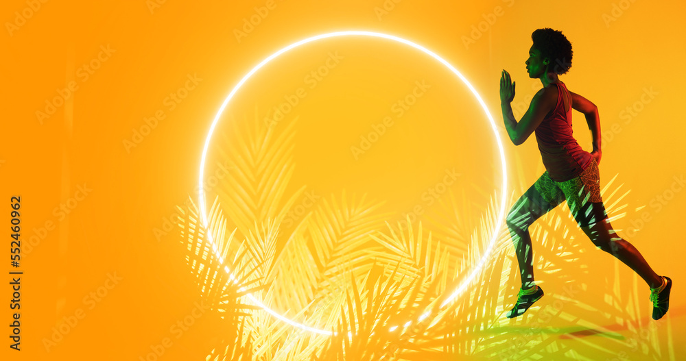 Side view of biracial female athlete running over illuminated circle and plants on yellow background