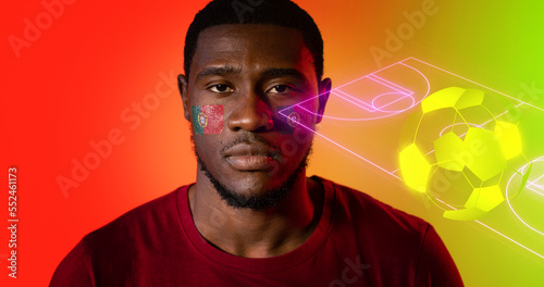 Portrait of african american man with portuguese flag's face paints by digital soccer field and ball