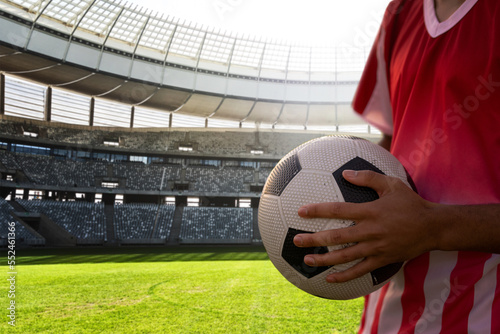 Midsection of player holding soccer ball in stadium on sunny day, copy space