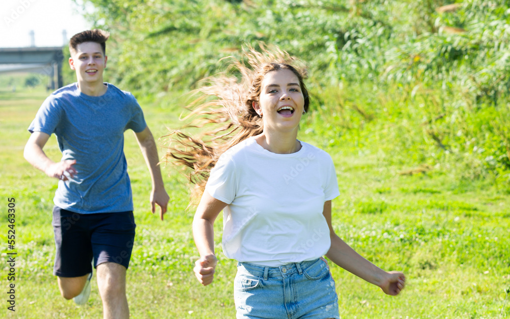 Obraz premium Laughing teenagers playing outdoors funning at grass on summer day