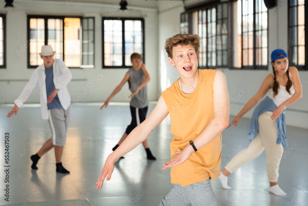 Emotional teen boy practicing active dance movements with friends at group dance class