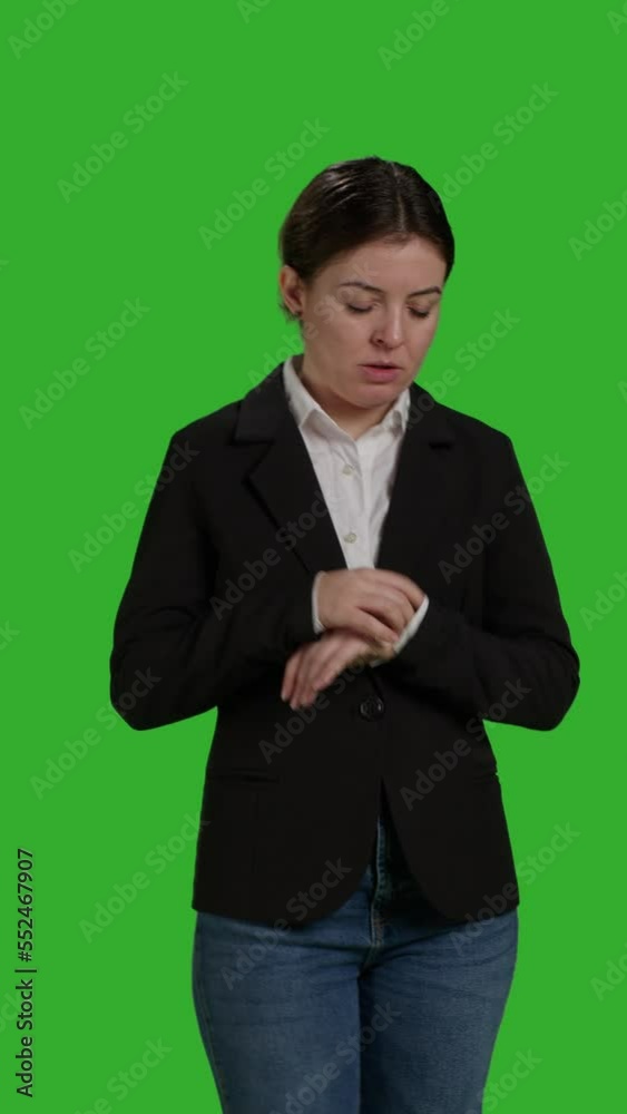 Vertical video: Front view close up of impatient office worker checking time on wristwatch, standing over isolated greenscreen backdrop. Young woman running late and looking at clock, waiting for Vertical video: Front view close up of impatient office worker checking time on wristwatch, standing over isolated greenscreen backdrop. Young woman running late and looking at clock, waiting for
