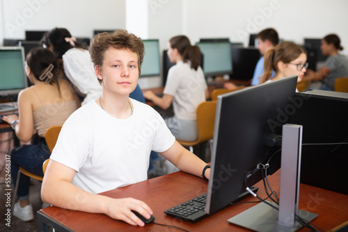 Portrait of smiling boy student looking at camera during lesson in computer class in college