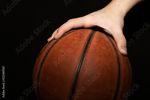 Basketball player holding the ball with one hand against a dark background close-up © Александр Ланевский