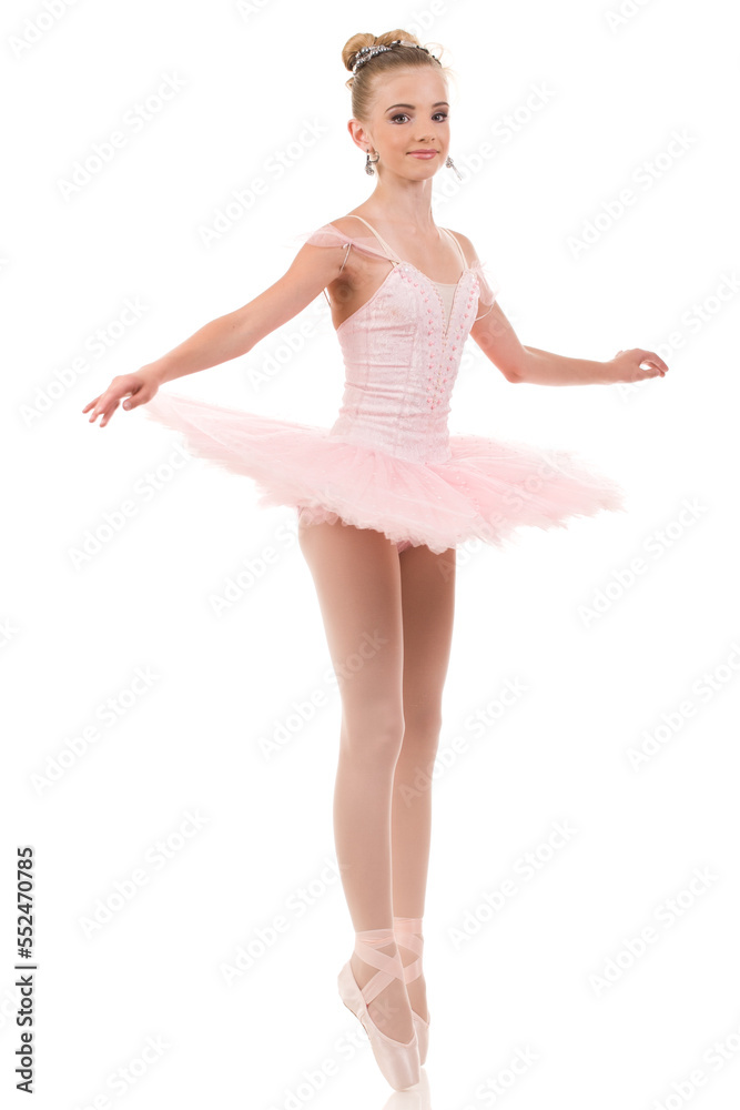 Young woman ballerina in white tutu, dancing on pointe with arms overhead, in the studio against a dark background.