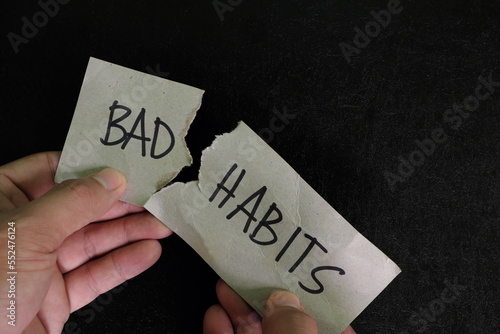 Breaking bad habits concept. Human hand tear a paper with word bad habit in dark black background. 
