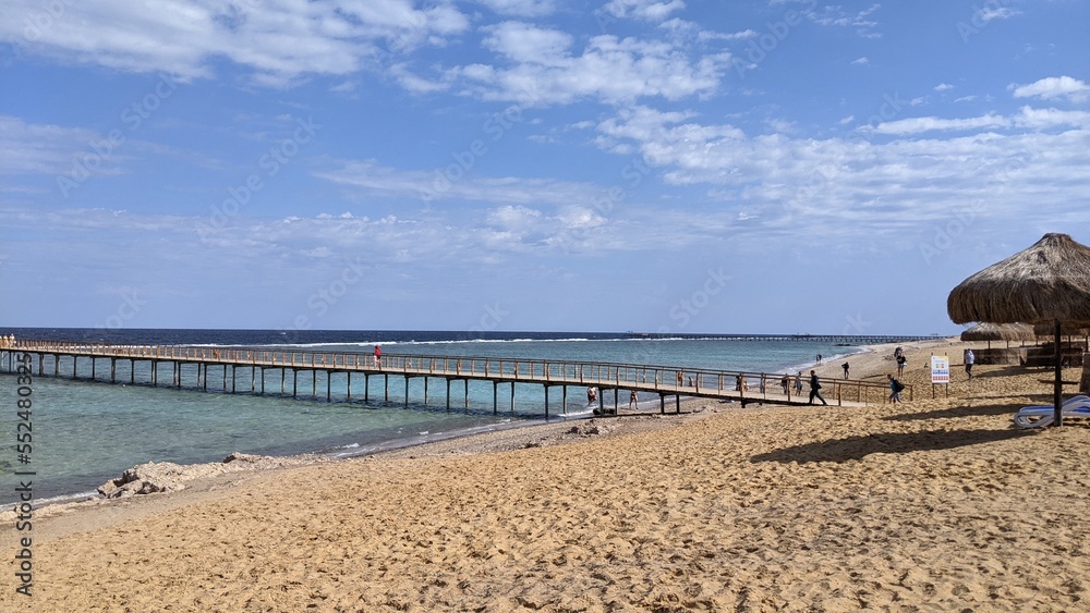wooden pier extending into the blue sea on a coral reef from a sandy shore

