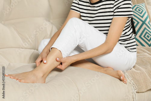 Woman rubbing sore leg on sofa, closeup