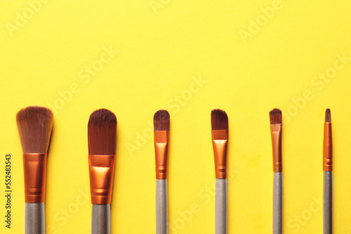 Different makeup brushes on yellow background, flat lay. Space for text