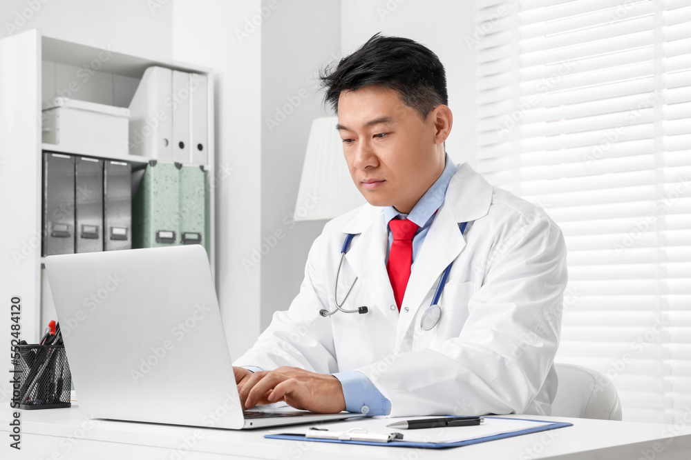 Doctor with laptop consulting patient at white desk in clinic. Online medicine Doctor with laptop consulting patient at white desk in clinic. Online medicine