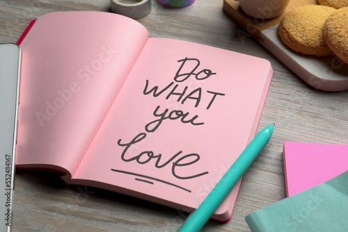 Open notebook with motivational phrase Do What You Love on wooden table