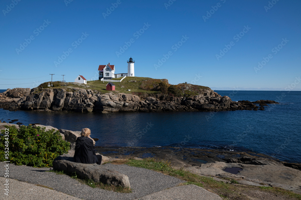 Woman sitting on a bench looking to the ocean at Nubble Lighthouse, York, Maine, USA Woman sitting on a bench looking to the ocean at Nubble Lighthouse, York, Maine, USA