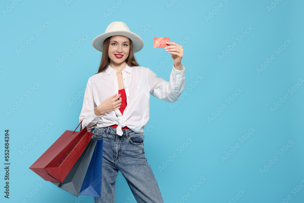 Stylish young woman with shopping bags and credit card on light blue background, space for text Stylish young woman with shopping bags and credit card on light blue background, space for text