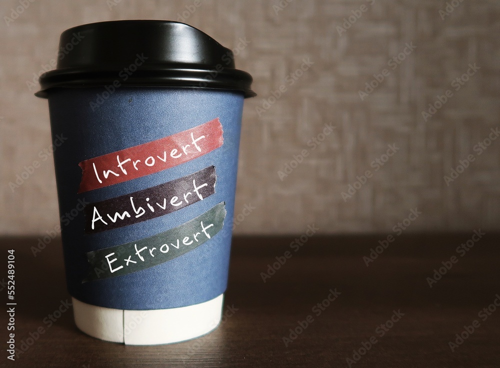 Paper coffee cup on copy space background with handwritten text - INTROVERT EXTROVERT AMBIVERT, Introverts tend to feel drained after socializing while extroverts tend to feel energized, ambivert is i Paper coffee cup on copy space background with handwritten text - INTROVERT EXTROVERT AMBIVERT, Introverts tend to feel drained after socializing while extroverts tend to feel energized, ambivert is i