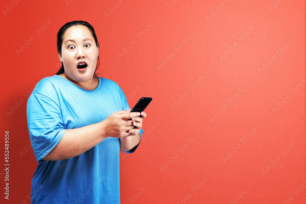Asian fat overweight woman holding a mobile phone with a shocked expression Asian fat overweight woman holding a mobile phone with a shocked expression