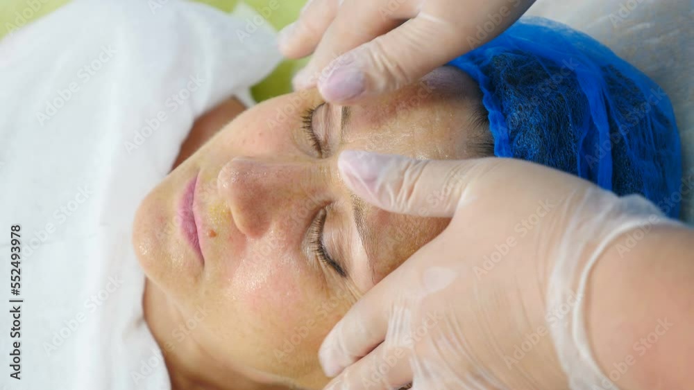 Beautician cosmetologist applies cosmetic product gel peeling mask with gloved hands, professional procedure in modern beauty clinic salon. Skincare and cosmetology spa. Top view. 4 k video