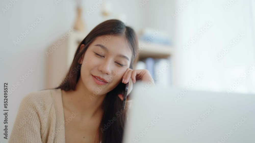 Young asian woman talking mobile smartphone while working on computer laptop on desk in living room at home Young asian woman talking mobile smartphone while working on computer laptop on desk in living room at home