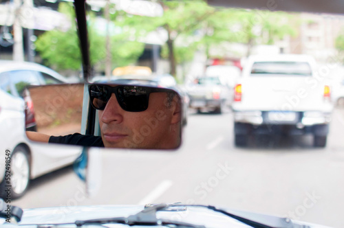 modelo homem em foto de rua com pose e expressão usando óculos sendo refletido no espelho do carro photo