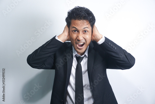 young handsome asian man looking angry, stressed and annoyed, covering both ears to a deafening noise, sound or loud music photo