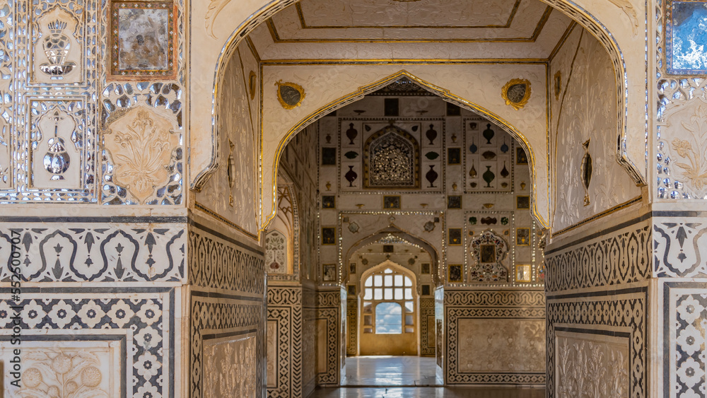 The interior of the famous mirror palace in the ancient Amber Fort. Arched openings, a barred window are visible. There are decorative paintings on the walls, mosaic ornaments made of mirror fragments