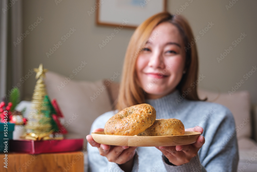 Portrait image of a young woman in sweater holding a plate of bagel with Christmas holiday decoration at home Portrait image of a young woman in sweater holding a plate of bagel with Christmas holiday decoration at home