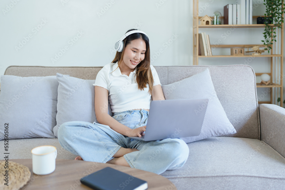 asian teenage girl using computer and wearing headphones at sofa