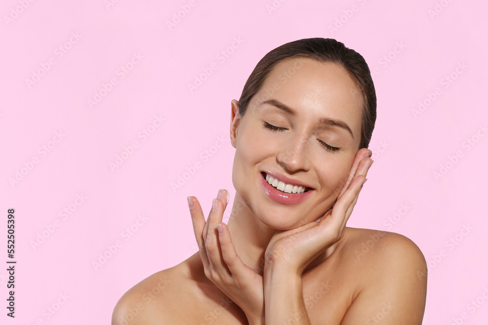 Studio portrait of young beautiful woman with long black hair tied in ponytail applying anti aging cream to her face. Close up, copy space, isolated pink background. Studio portrait of young beautiful woman with long black hair tied in ponytail applying anti aging cream to her face. Close up, copy space, isolated pink background.