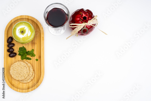 Festive background for Rosh Hashanah with free white space. Glass of red wine, black olives, green leaves, apple and pomegranate, traditional bread.