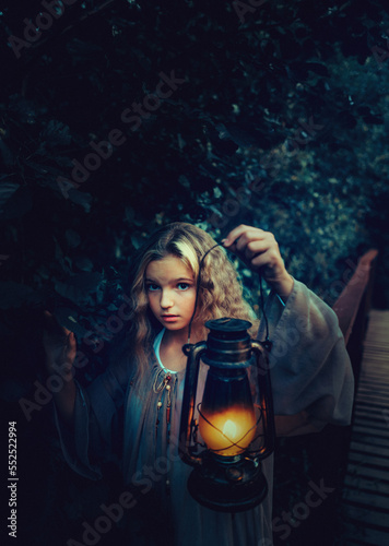 Girl with lantern in her hand standing on the wooden bridge in the night forest
