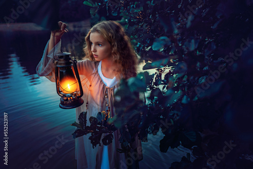 Girl with lantern in hand standing in the lake behind bushes at summer night