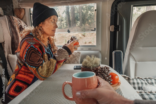 Happy couple enjoy time drinking tea inside a camper van. Nomadic lifestyle tourists people having relax leisure activity inside vehicle motor home. Renting vacation transport. Park outdoors view