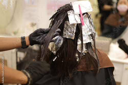 女性の髪に薬剤を塗布する男性美容師 © yamasan