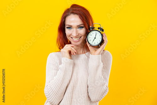Smiling Casual Winsome Ginger Head Girl Holding Alarm Watch Isolated Over Yellow Background