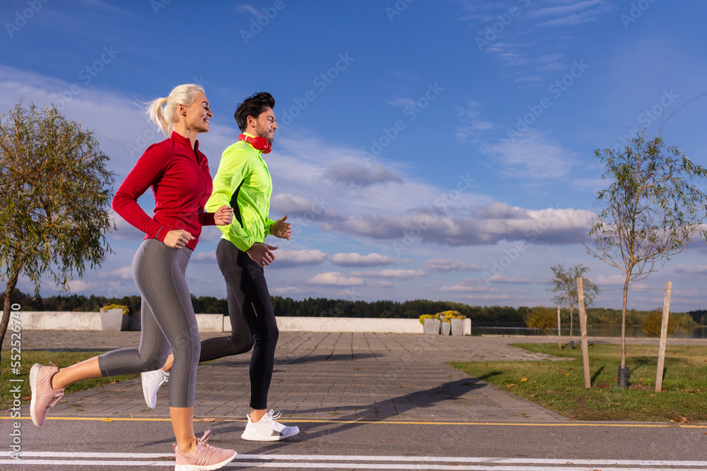 Sport Concepts. City Running Couple Happily Jogging Outside as Runners Training Outdoors Working Out in City As Fitness Couple Sport Concepts. City Running Couple Happily Jogging Outside as Runners Training Outdoors Working Out in City As Fitness Couple