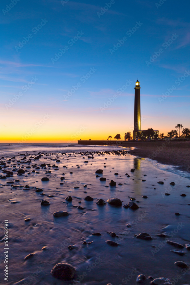 Travel Destinations. Lighthouse of Maspalomas At Gran canaria Island Known as  Faro de Maspalomas at Sunset During Blue Hour With Sea And Stones.