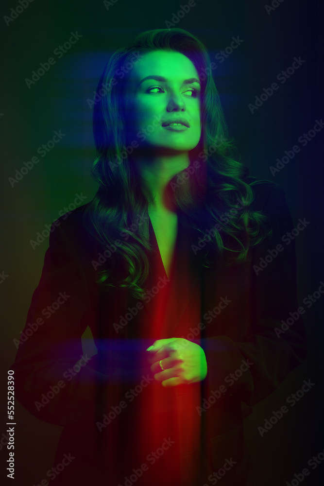 Pop art concept. Portrait of beautiful woman with dark suit and big wavy hair in red, green and blue color split effect. Model standing in grace pose and looking aside camera. Futuristic looking style