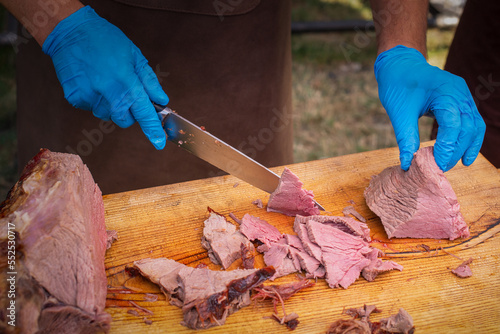 Hands of a male chef in blue gloves cutting a piece of grilled beef photo