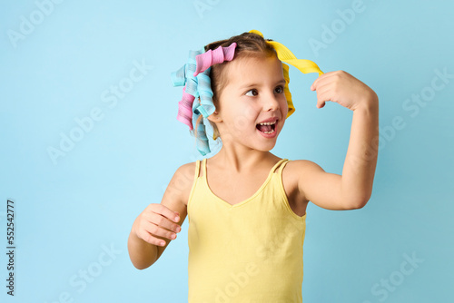 Little girl with curlers on blue background with copy space