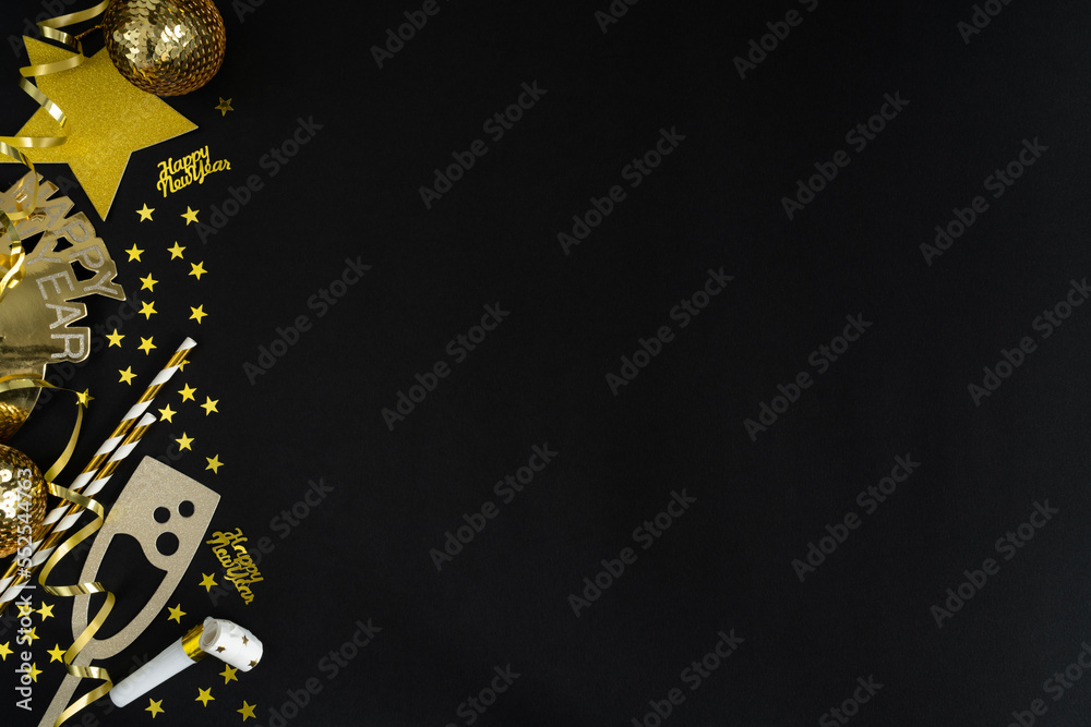 New Year's Eve party celebration. Golden decorations, confetti, streamers, horn blower. Happy New Year flat lay composition with copy space on black background.