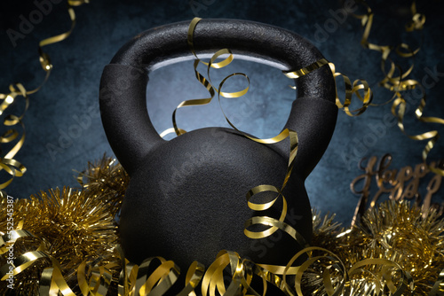 Heavy kettlebell and golden decorations, party streamers for New Year\'s Eve celebration, birthday or carnival. Healthy fitness lifestyle composition. Gym workout resolution, Happy New Year concept.