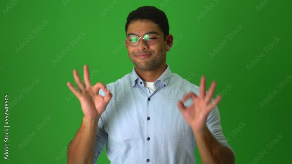 Happy Male Adult Shrugs, Points Finger, And Gestures Okay Hand Sign Against Green Backdrop. medium shot Happy Male Adult Shrugs, Points Finger, And Gestures Okay Hand Sign Against Green Backdrop. medium shot