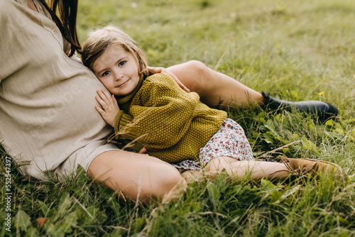 Little girl leaning on her pregnant mother belly, hugging, listening to what is inside the belly. Big sister concept.