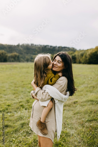 Pregnant woman and her toddler daughter hugging. Mother holding little girl in arms, spending fun time outdoors.