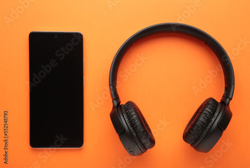 Black smartphone and wireless headphones on a orange background.