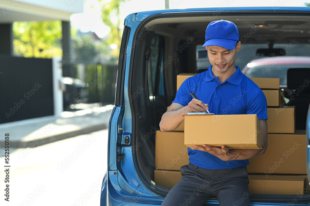 Man courier sitting in open delivery van and checking checking address details of client on clipboard Man courier sitting in open delivery van and checking checking address details of client on clipboard