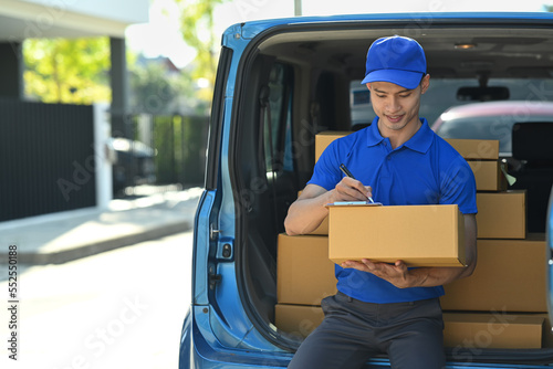 Man courier sitting in open delivery van and checking checking address details of client on clipboard